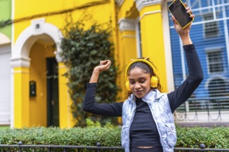 Happy african american woman dancing raising arms while listening to music with headphones and