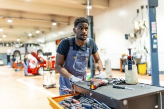 Young african car mechanic pushing a tool trolley in a busy workshop, preparing to repair a car