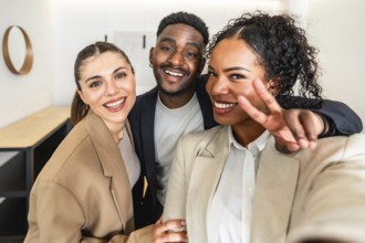 Three cheerful businesspeople taking a selfie, with one making victory sign, celebrating success in