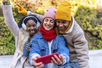Happy multi ethnic friends taking a selfie in a city park, enjoying a winter day together