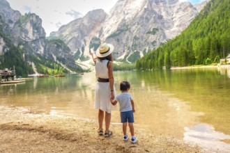 Mother pointing at the landscape while holding her son's hand on the shore of lake braies in the