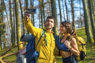 Couple taking a selfie with smartphone in the woods during camping trip, wearing backpacks and