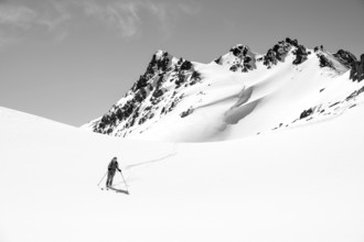 Ski tourer on the descent, minimalist winter landscape, white snow and dark mountains on the