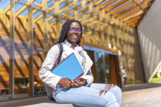 Female african student sitting outside the university and smiling at camera in a sunny day