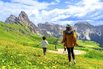 Tourists enjoying a sunny summer day walking through fields of wildflowers in seceda, dolomites,