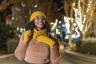 Smiling woman wearing winter clothes enjoying christmas lights decorating city trees at night