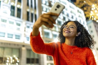 Smiling woman capturing a selfie with her mobile phone in a vibrant urban city, surrounded by