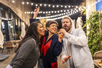 Happy multi-ethnic friends singing karaoke passionately during night party outdoors