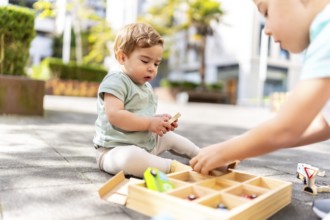 Close-up of two caucasian brothers playing with toys sitting in an urban park after school