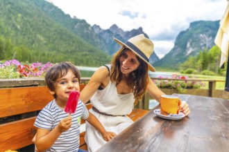 Mother and son enjoying a lakeside snack with a picturesque mountain backdrop in the dolomites