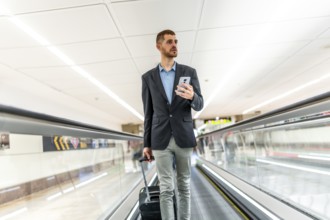 Businessman pulling suitcase and using smartphone while walking on moving walkway at airport