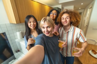 Four cheerful diverse friends are taking a selfie while enjoying juice in a modern kitchen