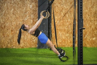 Side view of a Chinese strong woman exercising using gym rings in the cross training gym