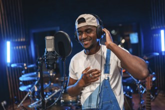 Young happy african american singer recording a song in professional music studio with blue lights