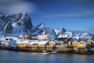 Traditional yellow rorbuer huts on the island of Sakrisøy, snow-capped mountains in the background,