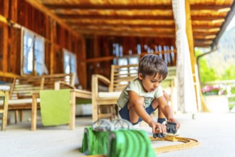 Child engaging with toy cars on a sunny outdoor porch surrounded by wooden furniture