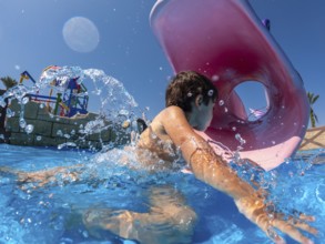 Child having fun swimming through inflatable ring in water park during summer vacation, enjoying