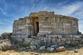 Ancient stone tower in ruins, surrounded by large rocks and blue sky, tomb of Cleovoulos the