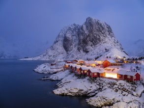 Rorbuer huts of Hamnoy at the fjord at dusk, snowy mountains in the background, Hamnøy, Reine,