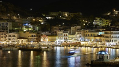 Night shot of a harbour with illuminated buildings and reflecting lights in the water, Pigadia,