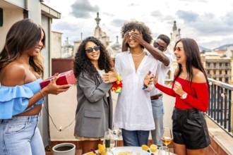 Multiracial group of friends covering eyes of a man giving her a present in a rooftop party