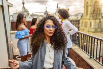 Cool woman in sunglasses smiling while friends partying on the background during rooftop evening