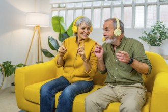 Cute senior couple listening to music together and dancing sitting on the sofa indoors
