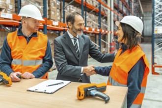 Manager and worker shaking hands in a logistics warehouse, smiling, with barcode readers and