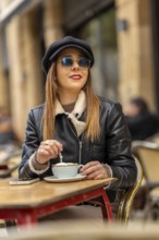 Fashionable woman wearing sunglasses and a hat savoring a cappuccino at a parisian cafe, enjoying