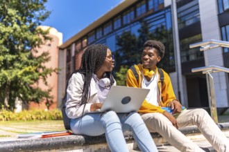 Two african american students using laptop sitting on the campus