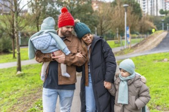Smiling parents walking with their children in a park on a chilly winter day, enjoying moments of