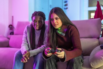 Two female friends enjoying their free time playing video games together on the sofa at home