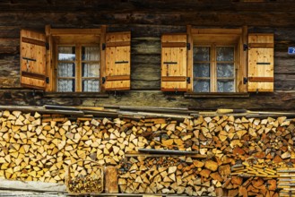 Old windows with shutters on an old farmhouse, firewood piled up in front, mountain village of