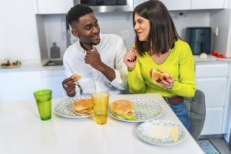 Young multiethnic couple sharing homemade burgers and enjoying each others company in a modern,