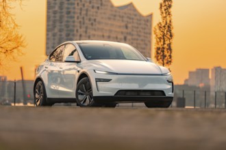White electric car in urban environment with modern architecture and sunset, Tesla New Model Y,