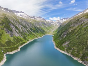 Mountain landscape with a blue lake in the centre, surrounded by lush greenery and snow-capped