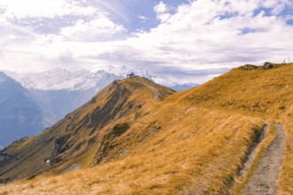 A narrow path leads over an autumnal mountain ridge under a cloudy sky, Planplatten, Switzerland,