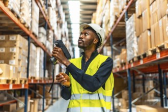 African american manual worker in reflective clothes scanning parcels in a warehouse full of boxes