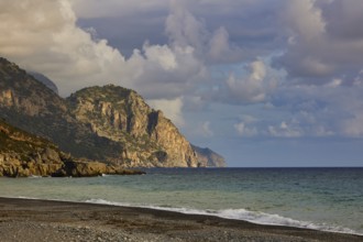 Rocky cliffs on the coast with foamy waves and a dramatic cloudy sky in the distance, south coast,
