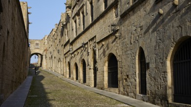 An ancient street lined with historic buildings with arcades in sunny weather and blue skies, moped
