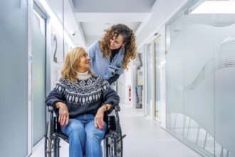 Young tender nurse talking to a mature injured woman in wheelchair in the hospital