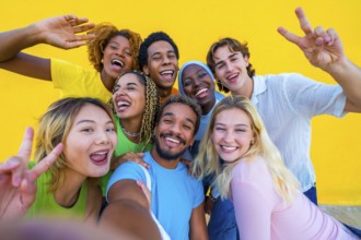 Multi-ethnic friends gesturing peace while taking a selfie next to a yellow wall