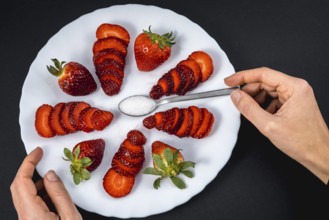 A woman's hand in a overhead view of natural strawberries on a white plate