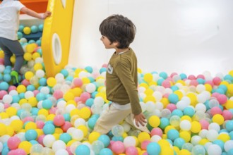 Young boy joyfully playing in a vibrant ball pit, surrounded by a colorful playground that sparks