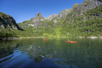 Two kayakers with red kayaks in the fjord Trollfjord, mountain peaks are reflected in the water,