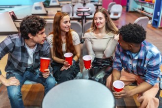 Four young friends enjoying a casual hangout at the bowling alley, holding red cups and engaging in