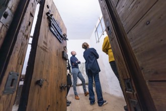 Several people standing in a room with large wooden doors and a historical appearance, Prison