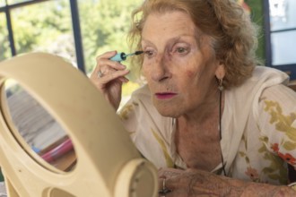 Senior woman applying mascara while gazing into a mirror, preparing for an outing. Embracing her