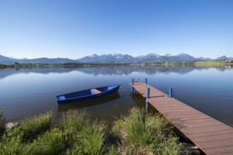 Blue sky over an alpine lake with a boat and a jetty, surrounded by mountains, Hopfen am See, near