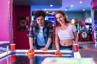 Multiethnic friends enjoying a weekend together, playing air hockey in a vibrant entertainment